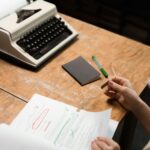 A person reviews a document at a desk with a retro typewriter, emphasizing office work in a vintage setting.